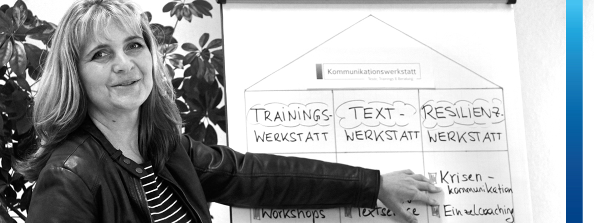 Frau zeigt auf Flipchart mit dem Text Trainingswerkstatt, Textwerkstatt , Resilienzwerkstatt und Krisenkommunikation